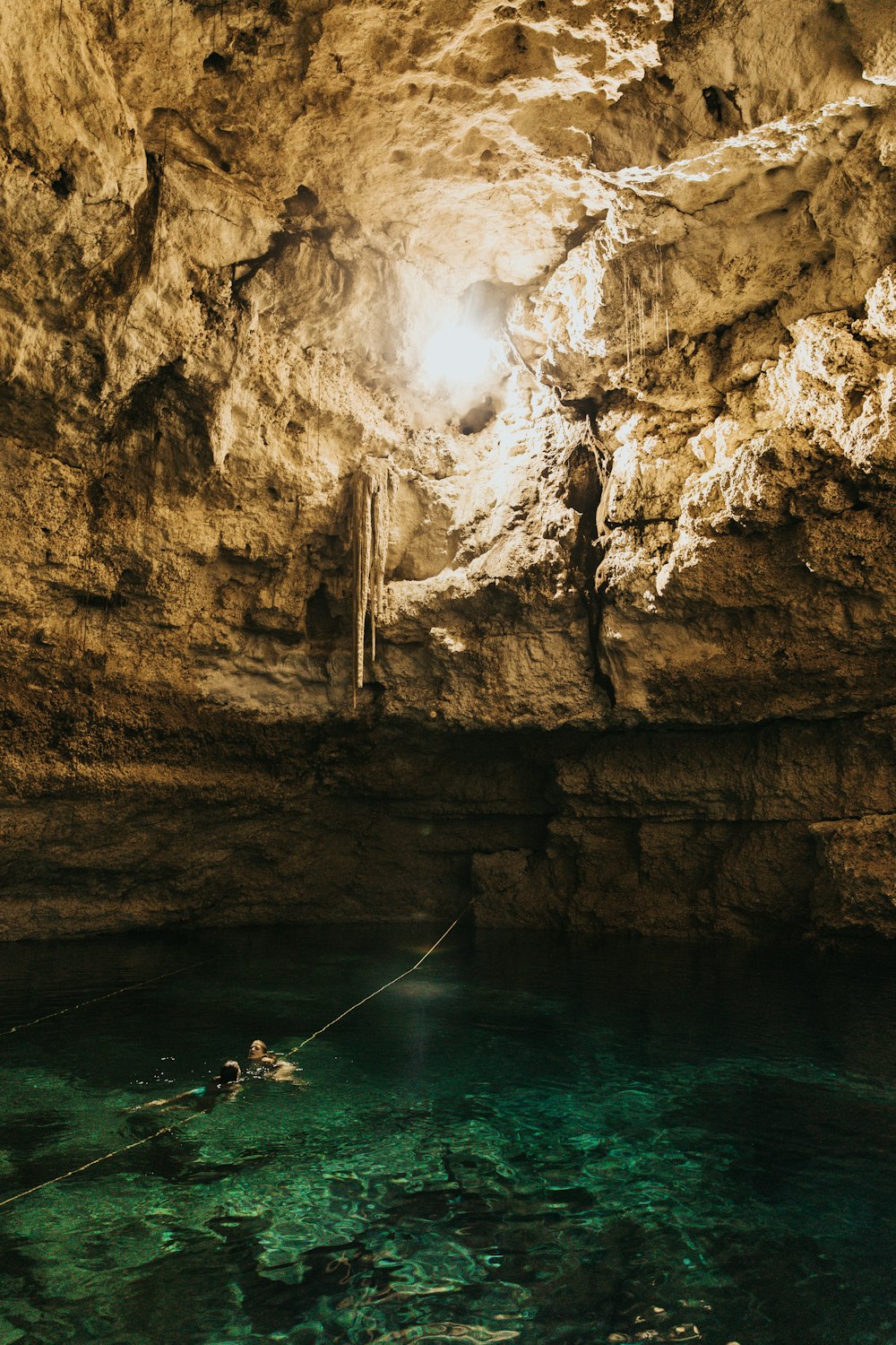 two person swimming in body of water inside cave during daytime