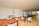 A spacious indoor recreational area with wooden flooring, featuring a foosball table, ping pong tables, and wooden tables and chairs. Large windows line one wall, allowing natural light to fill the space.