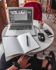 A warm, inviting workspace with a laptop displaying marriina.com on the screen, surrounded by notes and a coffee cup.