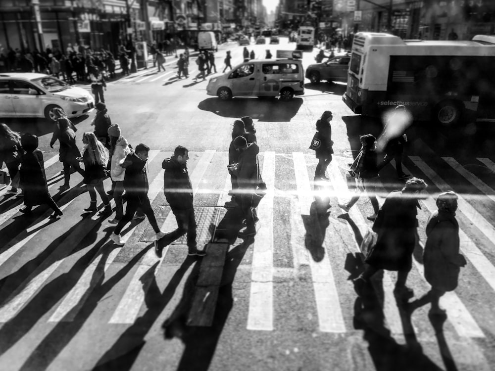 foto em tons de cinza de pessoas passando na faixa de pedestres durante o dia