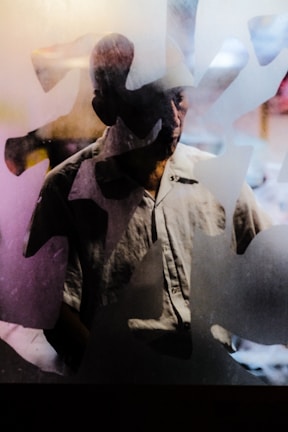 A person is partially visible behind a frosted glass or translucent surface, creating an abstract and mysterious effect. The lighting casts shadows and highlights, emphasizing the texture of the glass and the person's silhouette.
