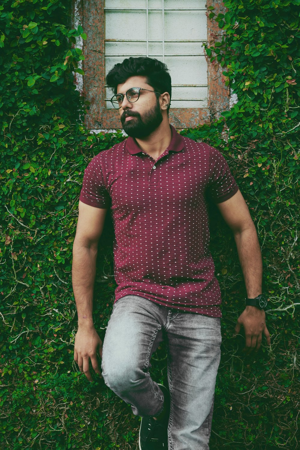 man in maroon polo shirt leaning on wall and green plants