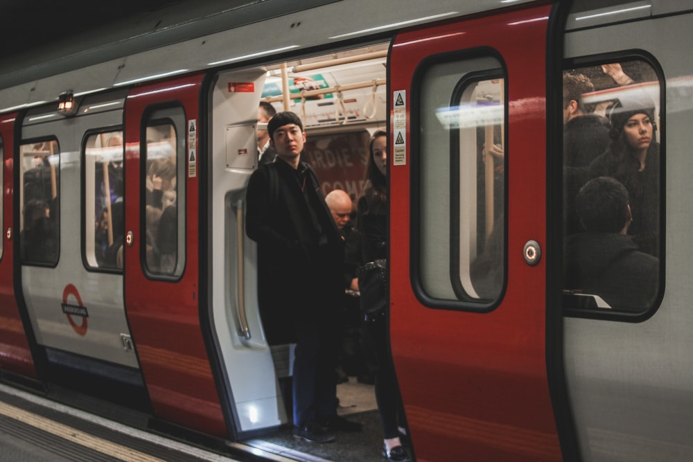 Un hombre parado en una plataforma de tren junto a un tren rojo y plateado