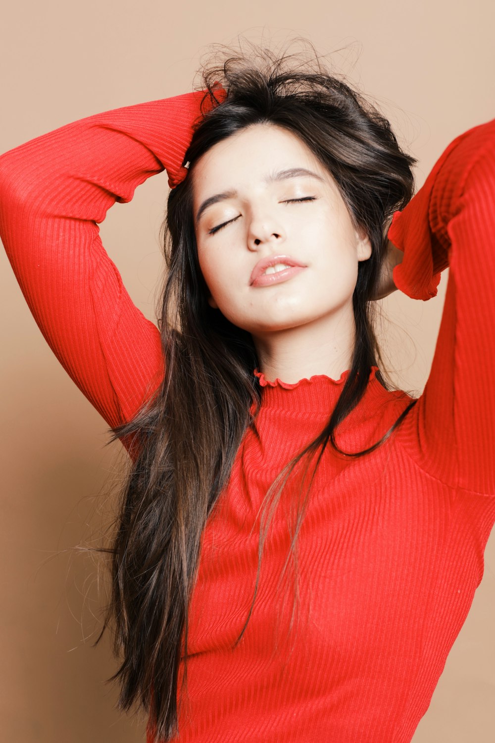 woman in red turtleneck sweater holding her hair and closing eyes