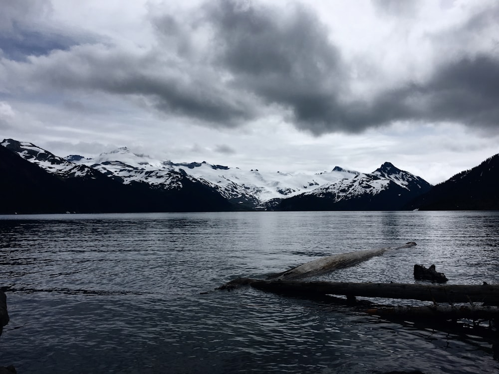 grayscale photography of calm water near ice-capped mountain