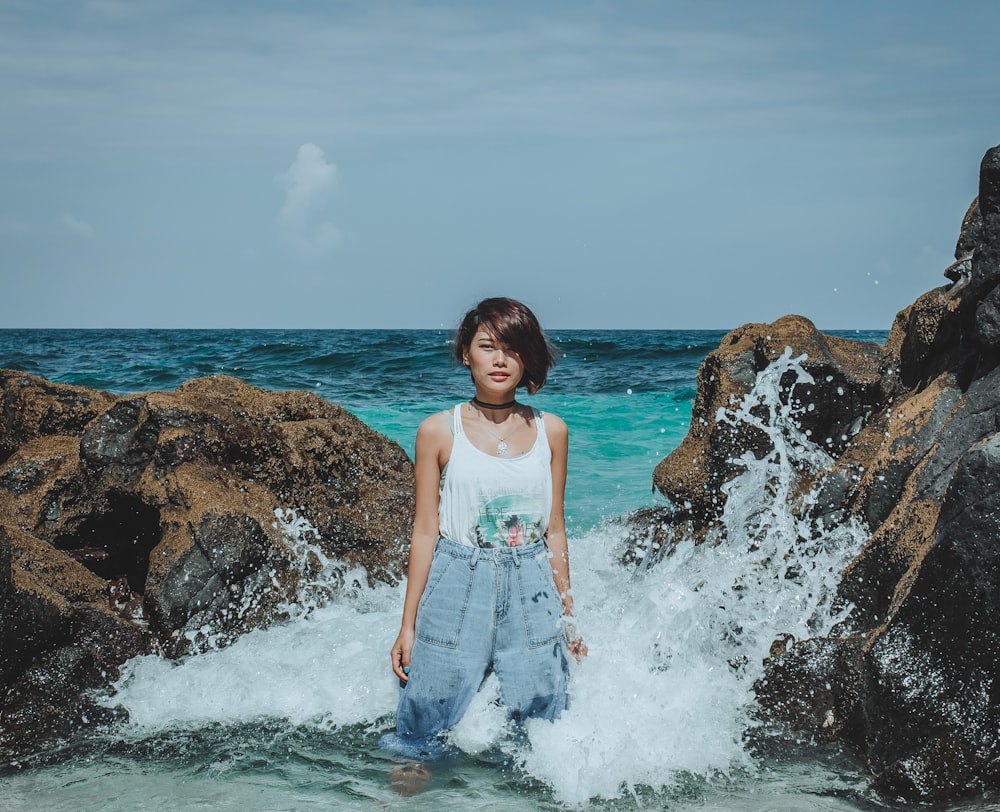 woman in white tank top standing beside rocks on body of water