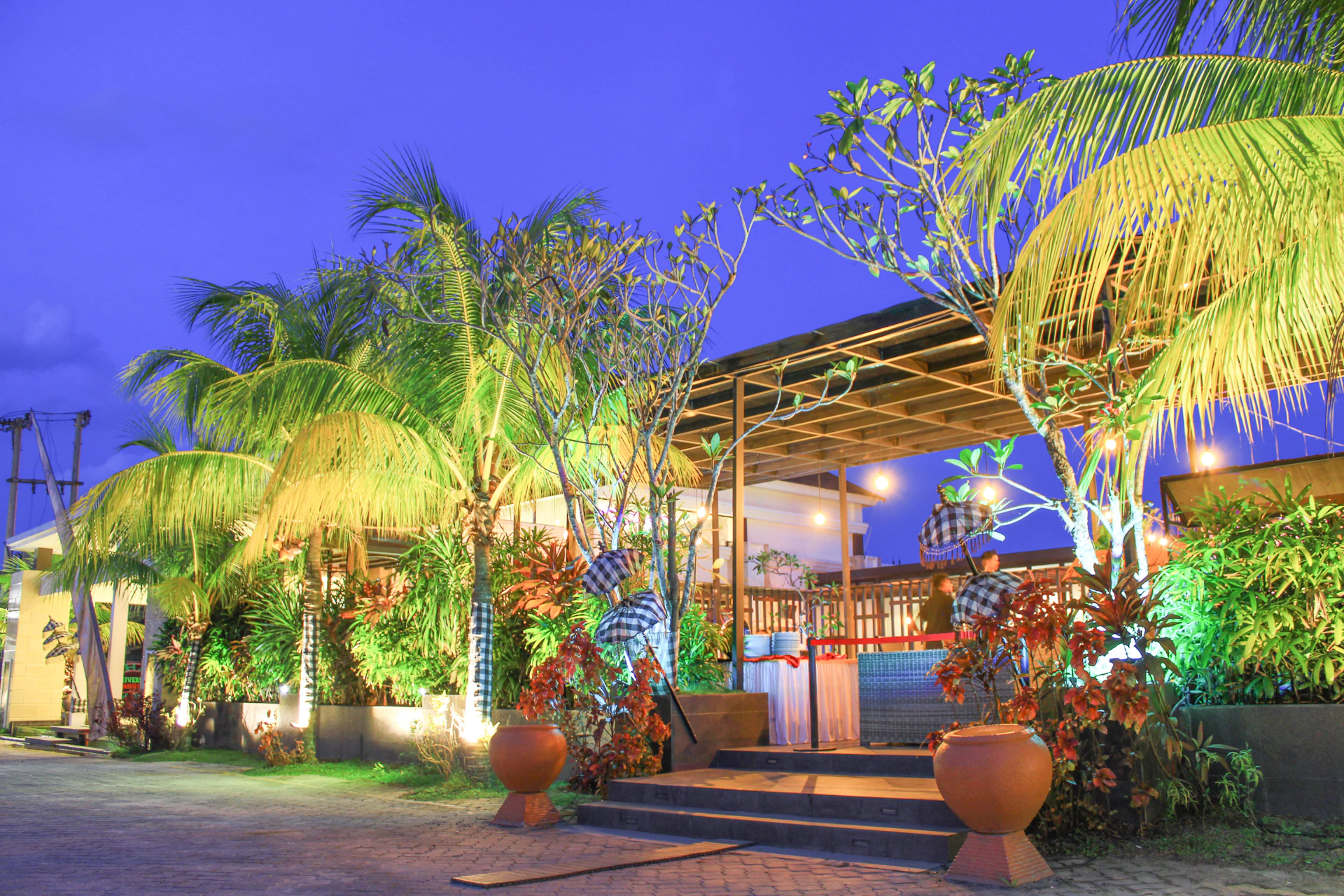 Evening scene of Palmeras Lounge Bar's outdoor seating area with soft beige lighting and lush palm plants.