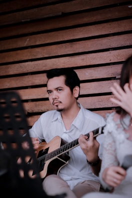A musician playing an acoustic guitar with a peaceful expression in a studio.