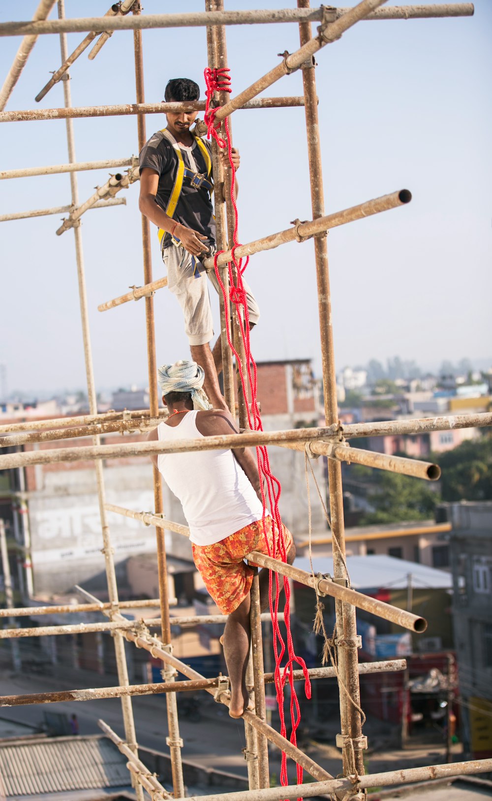 two men climbing on brown bamboo scaffolding at daytime