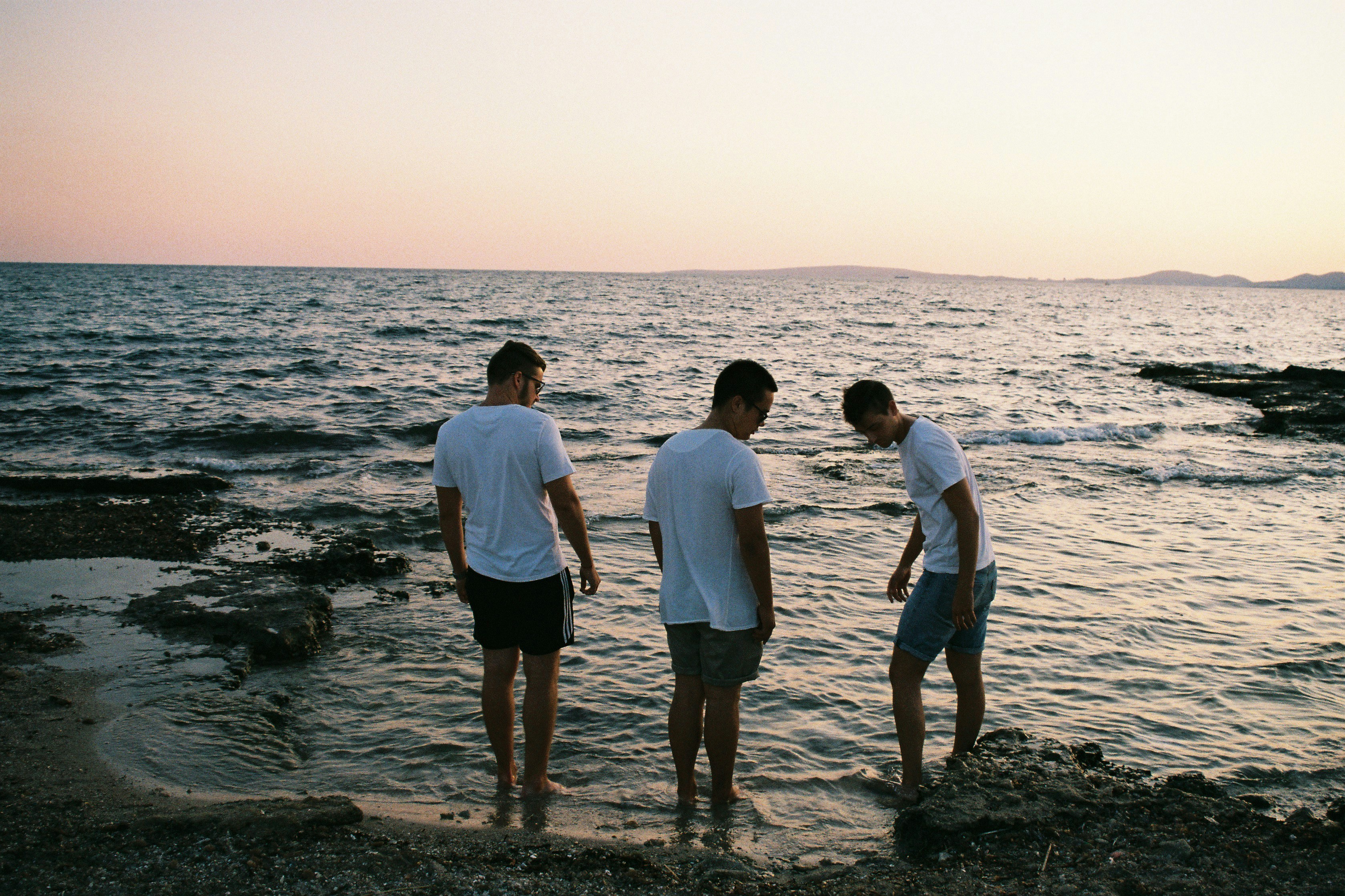 tre uomini che indossano camicie bianche in piedi sulla riva del mare