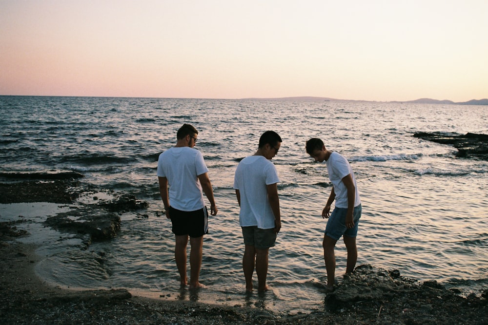 three men wearing white shirts standing on seashore
