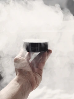 Hands holding an oceánika speaker with sound waves artistically blending with ocean spray