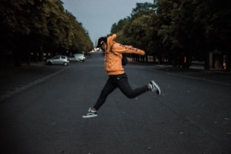 person in orange hoodie jumping on middle of road