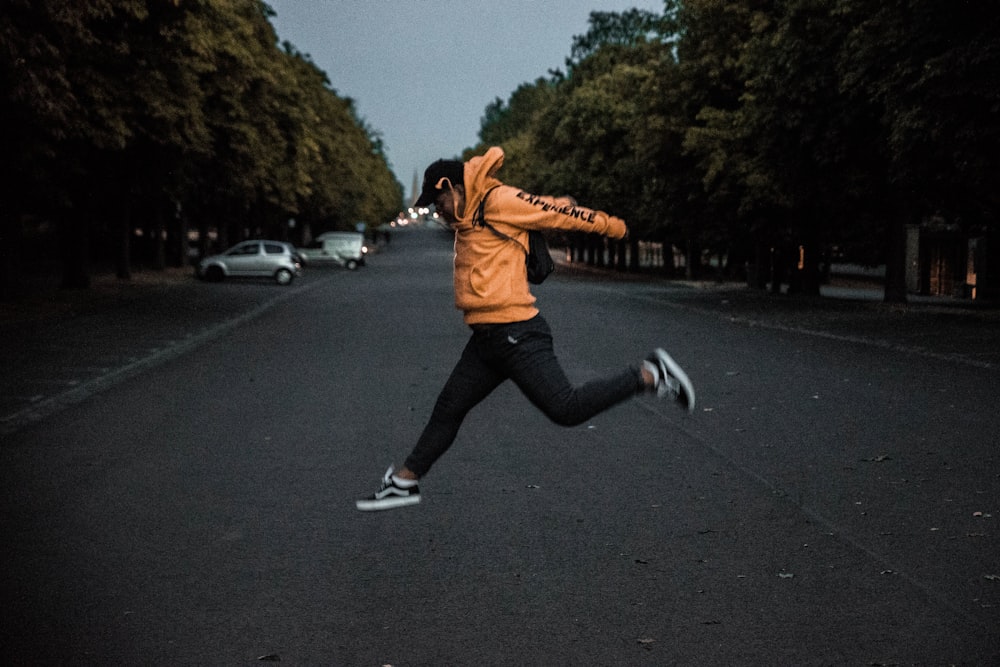 person in orange hoodie jumping on middle of road