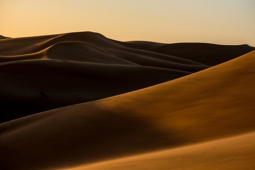 the sun is setting over a desert with sand dunes