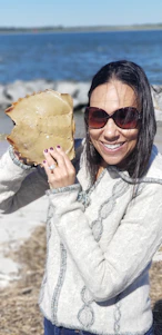 A smiling woman holding a fresh fish at a rustic seaside fish market.