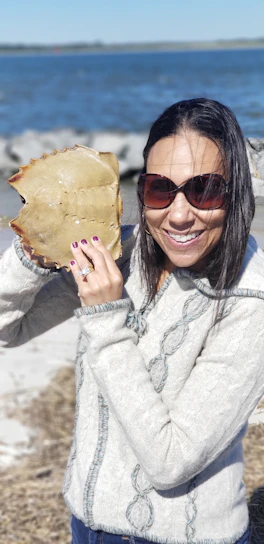 A smiling woman holding a fresh fish at a rustic seaside fish market.