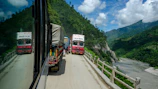 A convoy of trucks driving through a scenic European mountain road