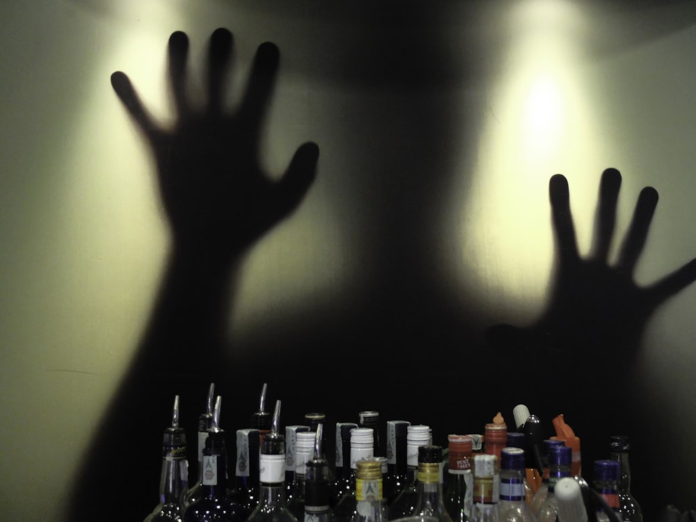 assorted-brand glass bottles with shadows of man behind glass