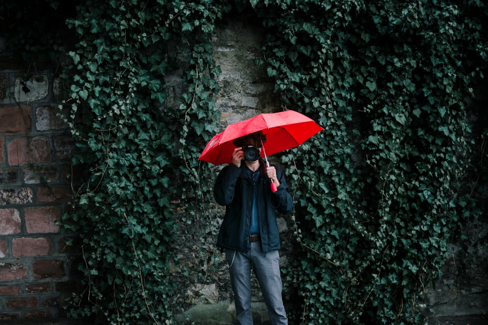 man wearing black jacket holding red umbrella