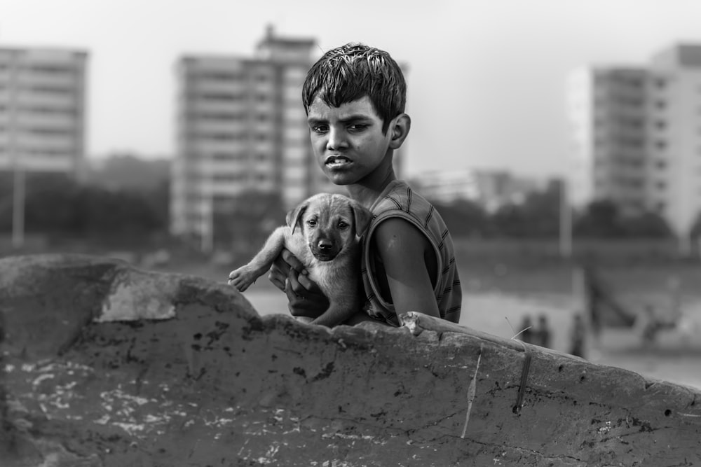 boy on sleeveless top holding puppy black and white photography