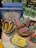 A selection of decorative items including Christmas-themed ornaments resembling butter sticks, cookies, and crackers are displayed. A series of cookbooks titled 'Betty Crocker Lost Recipes' are stacked in the background. An assortment of kitchenware, including salt and pepper shakers, is also visible.