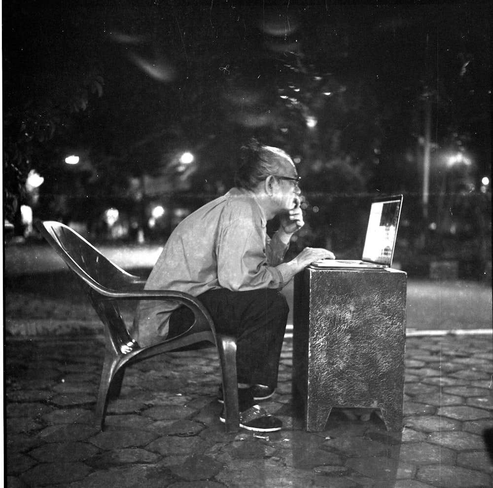 man sitting on chair infront of table while looking at laptop