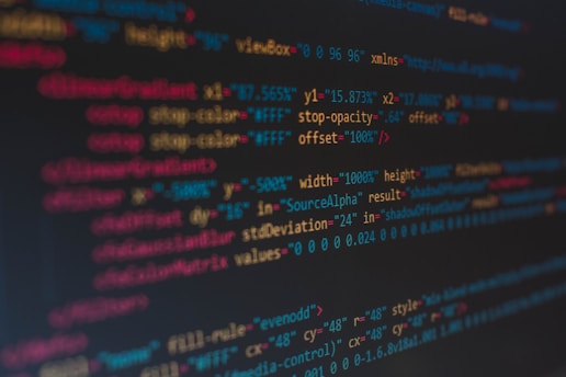 A close-up view of colorful HTML and CSS code displayed on a computer screen. The lines of code are predominantly highlighted in shades of blue, red, orange, and yellow on a dark background, indicating syntax highlighting for readability.