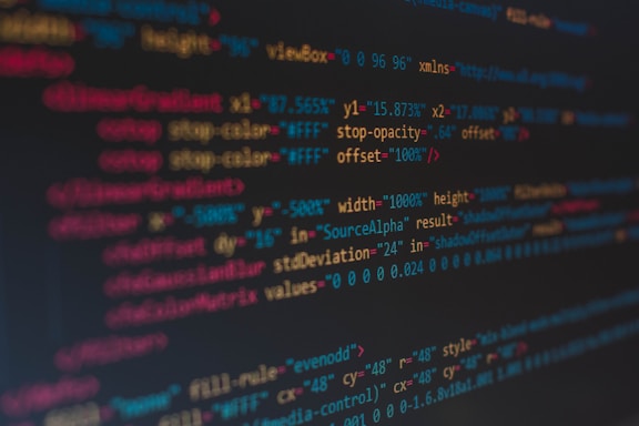 A close-up view of colorful HTML and CSS code displayed on a computer screen. The lines of code are predominantly highlighted in shades of blue, red, orange, and yellow on a dark background, indicating syntax highlighting for readability.