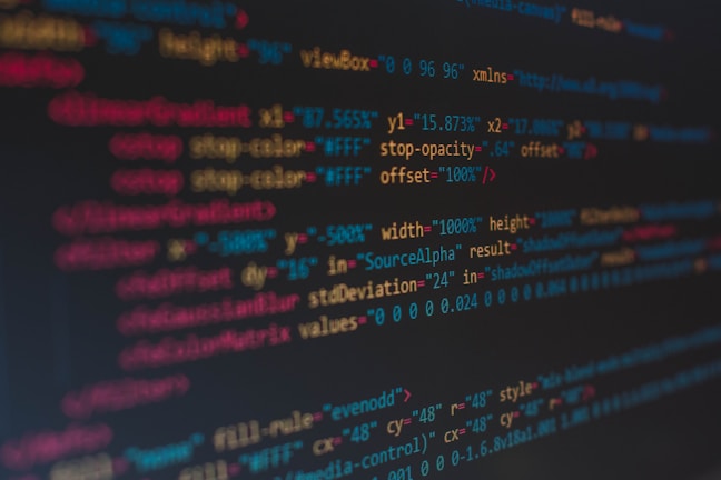 A close-up view of colorful HTML and CSS code displayed on a computer screen. The lines of code are predominantly highlighted in shades of blue, red, orange, and yellow on a dark background, indicating syntax highlighting for readability.