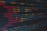 A close-up view of colorful HTML and CSS code displayed on a computer screen. The lines of code are predominantly highlighted in shades of blue, red, orange, and yellow on a dark background, indicating syntax highlighting for readability.