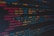 A close-up view of colorful HTML and CSS code displayed on a computer screen. The lines of code are predominantly highlighted in shades of blue, red, orange, and yellow on a dark background, indicating syntax highlighting for readability.