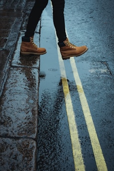 person wearing brown boots walking on a wet road