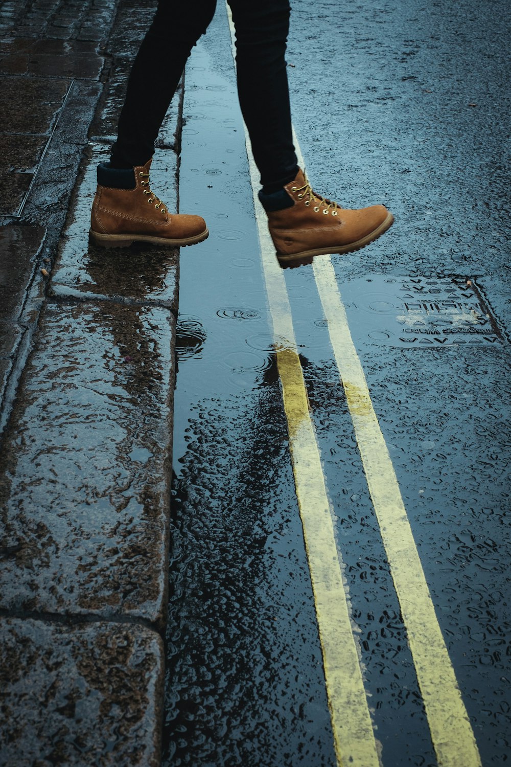 Person mit braunen Stiefeln, die auf einer nassen Straße geht