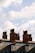 Several brick chimneys rise above a row of traditional slate-roofed buildings. The chimneys vary in size and are topped with multiple clay chimney pots. The sky is filled with fluffy, white clouds against a pale blue backdrop.