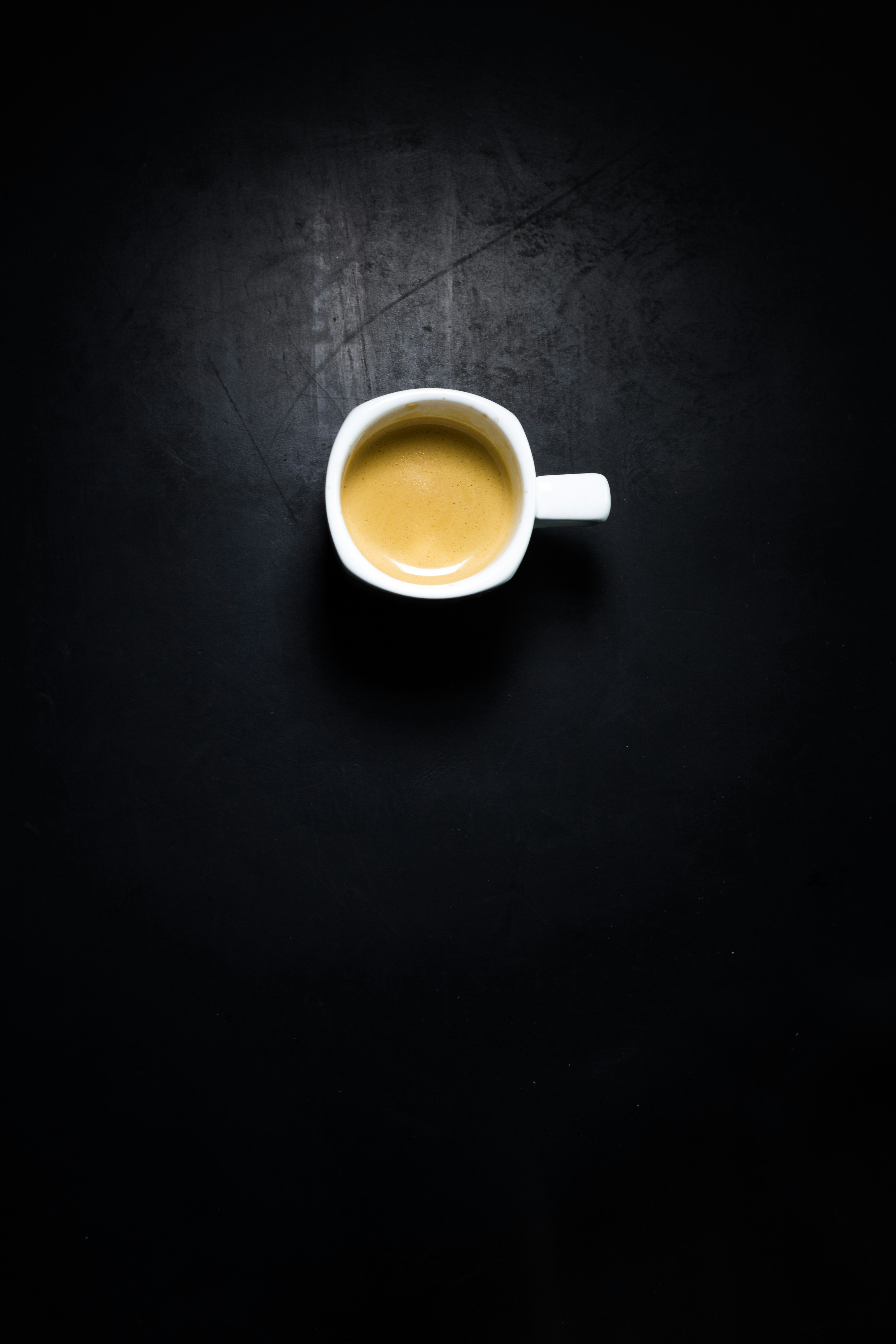 Rich dark espresso shot in white ceramic cup, dark coffee crema on top, moody dark cafe background