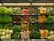 A variety of fresh vegetables are neatly arranged on multiple shelves in a grocery store. The assortment includes leafy greens, red and yellow bell peppers, zucchinis, yellow squash, eggplants, and cauliflower. The produce is organized in rows with similar items grouped together, showcasing vibrant colors and freshness under the store's lighting.