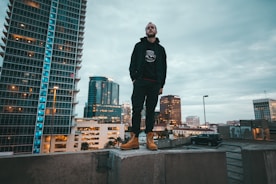 A confident individual standing on a rooftop overlooking a city skyline at sunrise.