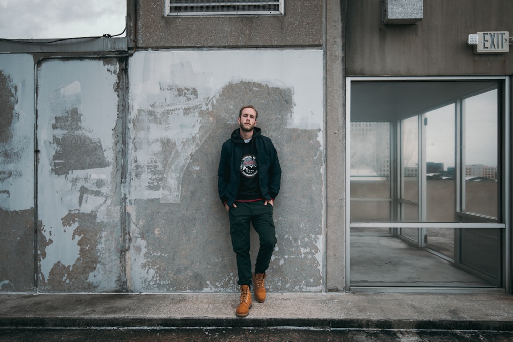 man leaning on wall with both hand on pocket