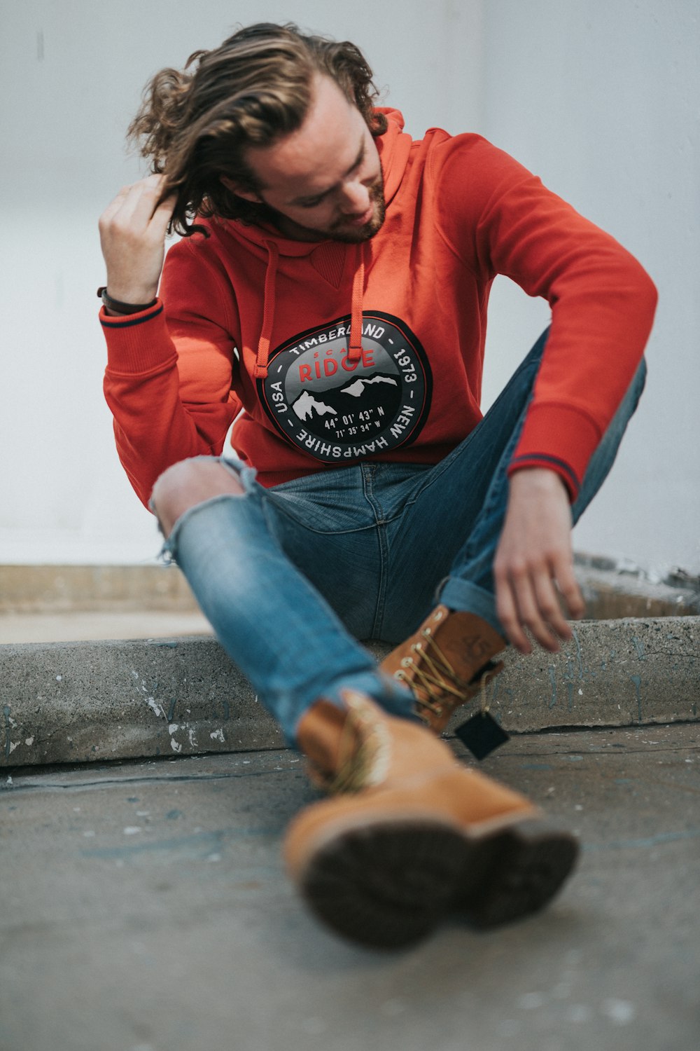 man in orange hoodie sitting on gray pavement during daytime