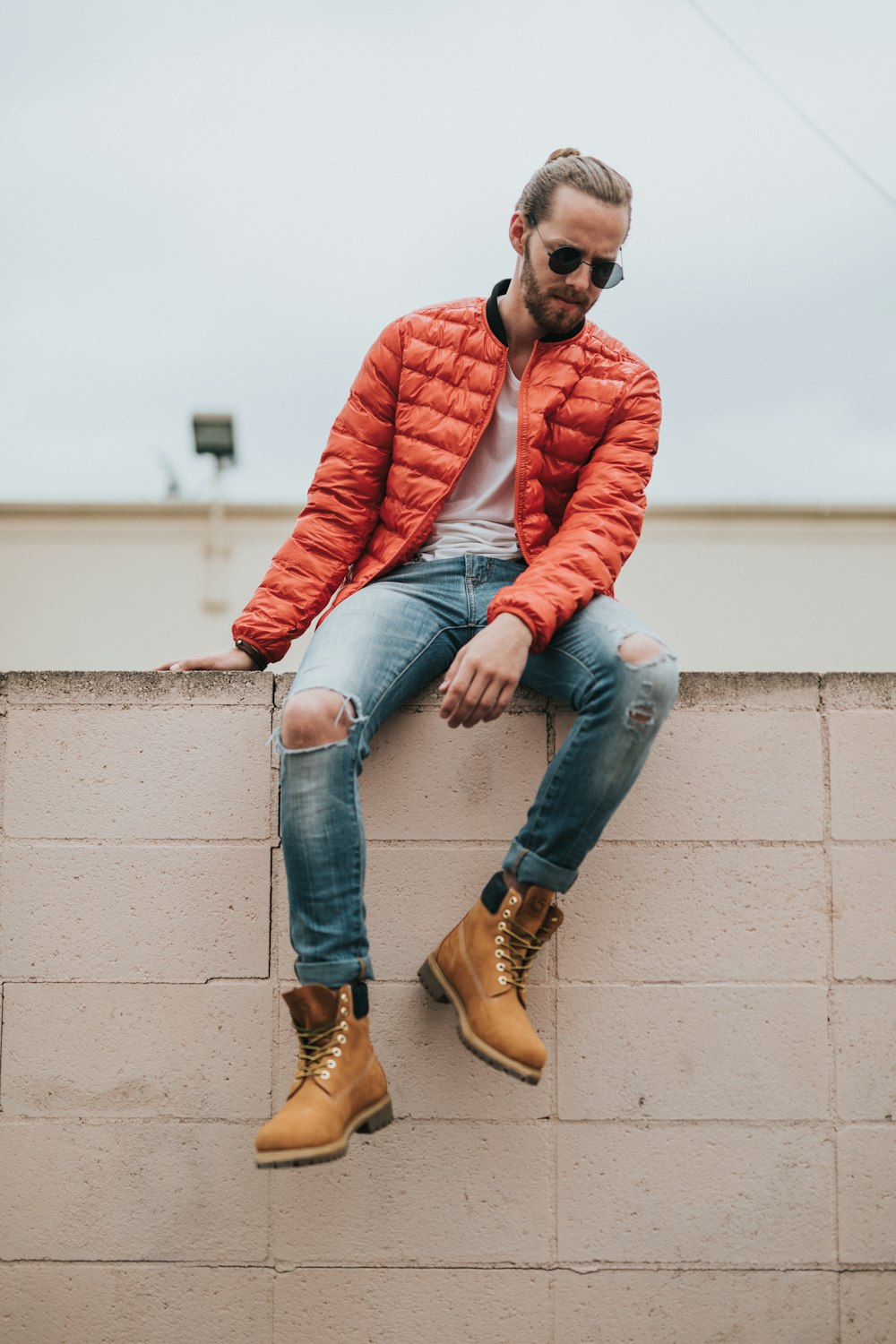 벽에 앉아있는 주황색 버블 재킷을 입은 남자