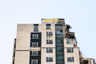 A partially demolished high-rise building with visible rubble on the right side, and graffiti such as 'VOID' and 'CARF' on the windows. The structure appears worn and neglected, suggesting abandonment or urban decay.