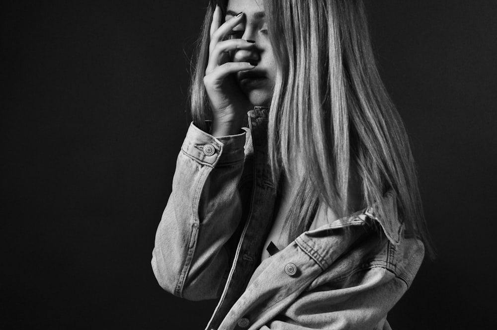 woman in denim jacket covering her face with her palm