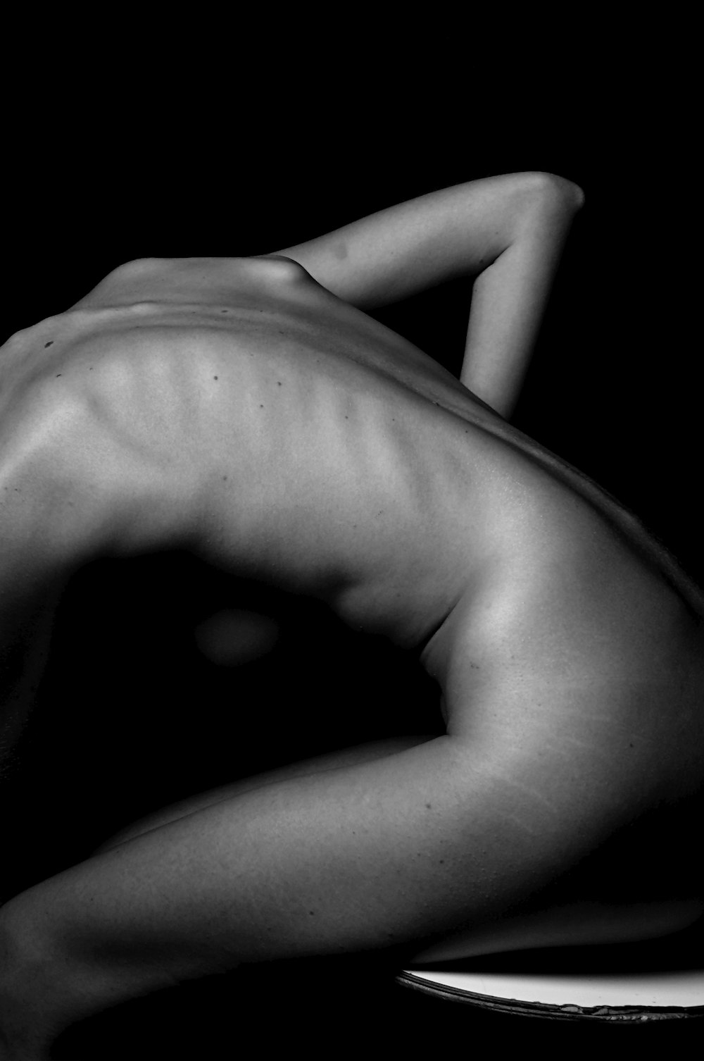 una mujer desnuda sentada en una mesa de espaldas a la cámara