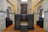 A historic interior with stone walls and wooden pews in rows along the sides. A dark wooden bimah with ornate carvings sits at the center, surrounded by arches and stonework, suggesting a religious setting.