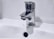 A chrome faucet is mounted on a white sink. A small stream of water is dripping from the tap's spout into the basin below. The background is a plain light color, enhancing the metallic shine of the faucet.