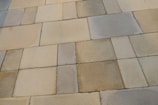 A series of rectangular stone tiles with varying shades of beige, gray, and brown create a patchwork pattern. The texture of the stones is slightly rough, indicating a natural material often used for outdoor flooring or walkways.