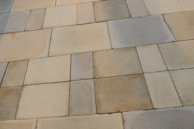 A series of rectangular stone tiles with varying shades of beige, gray, and brown create a patchwork pattern. The texture of the stones is slightly rough, indicating a natural material often used for outdoor flooring or walkways.