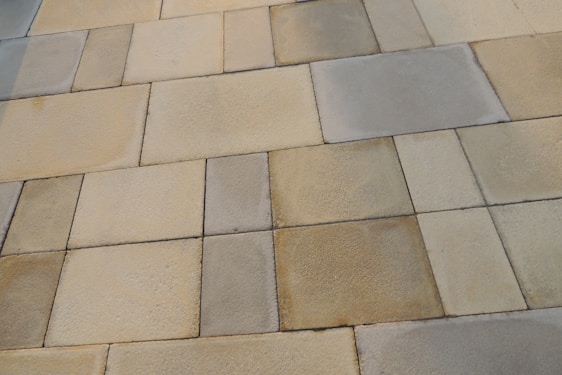A series of rectangular stone tiles with varying shades of beige, gray, and brown create a patchwork pattern. The texture of the stones is slightly rough, indicating a natural material often used for outdoor flooring or walkways.