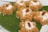 Seven pieces of a brown-colored dessert made from vermicelli or a similar ingredient are arranged on a large green leaf. Each dessert piece is topped with a sprinkle of grated white coconut and has a single raisin in the center.